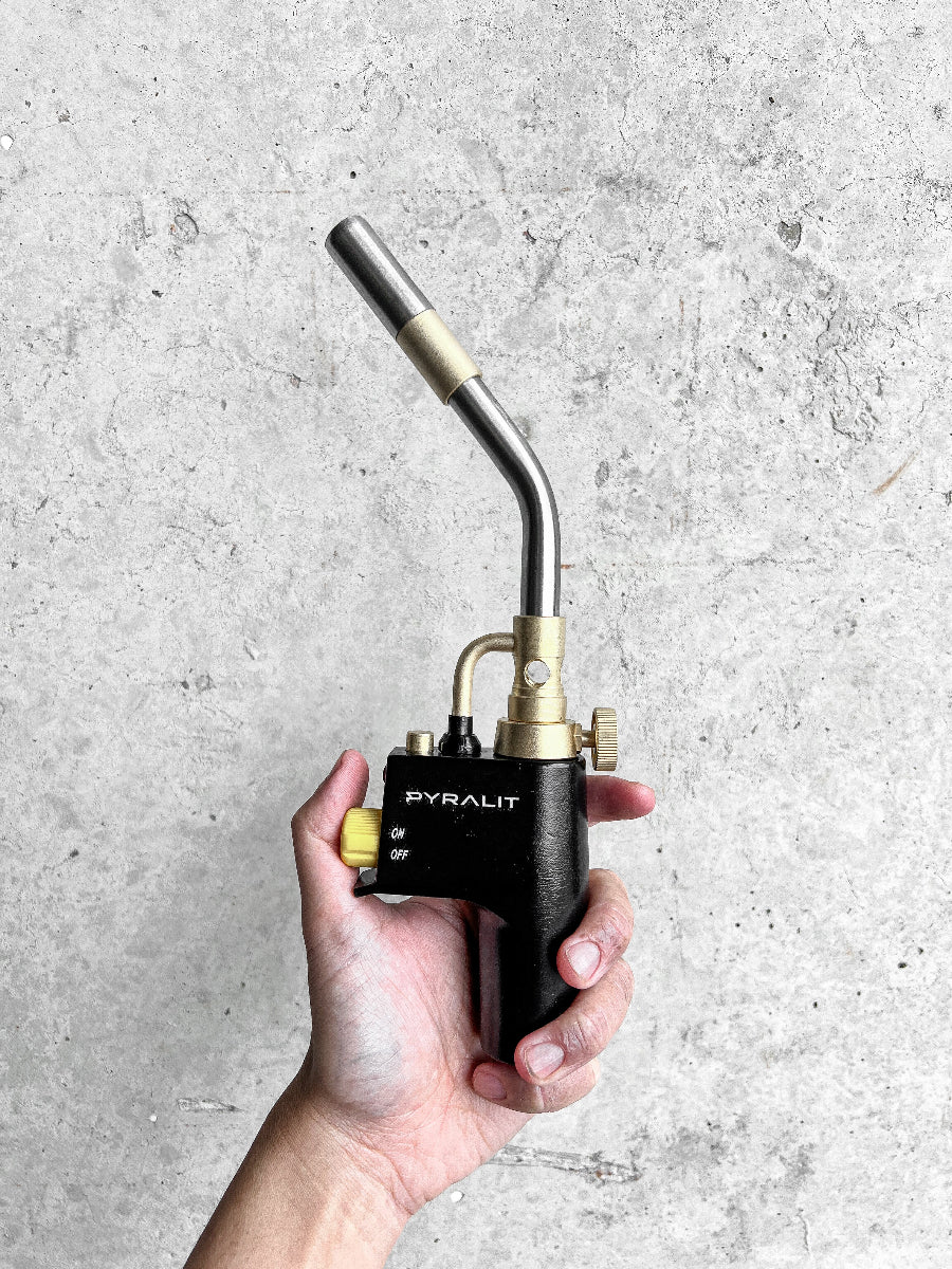 Hand holding a Pyralit torch against a gray concrete background