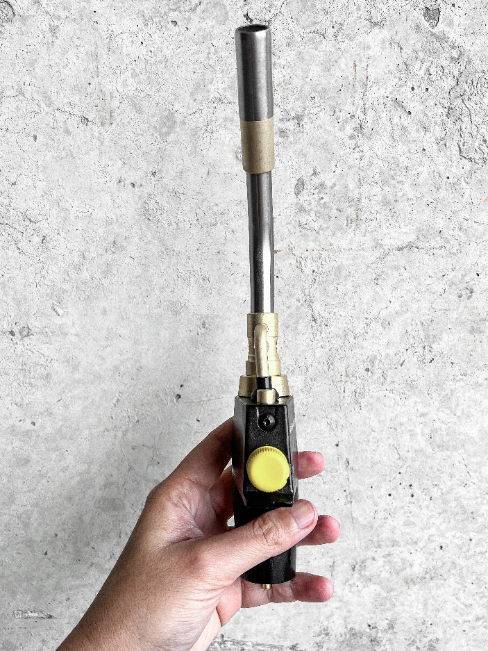 Hand holding a small torch against a gray concrete background