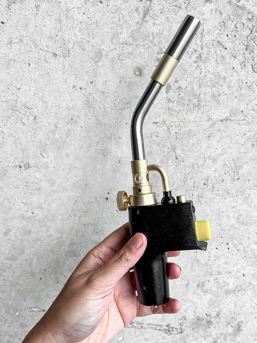 Hand holding a butane torch against a gray concrete background