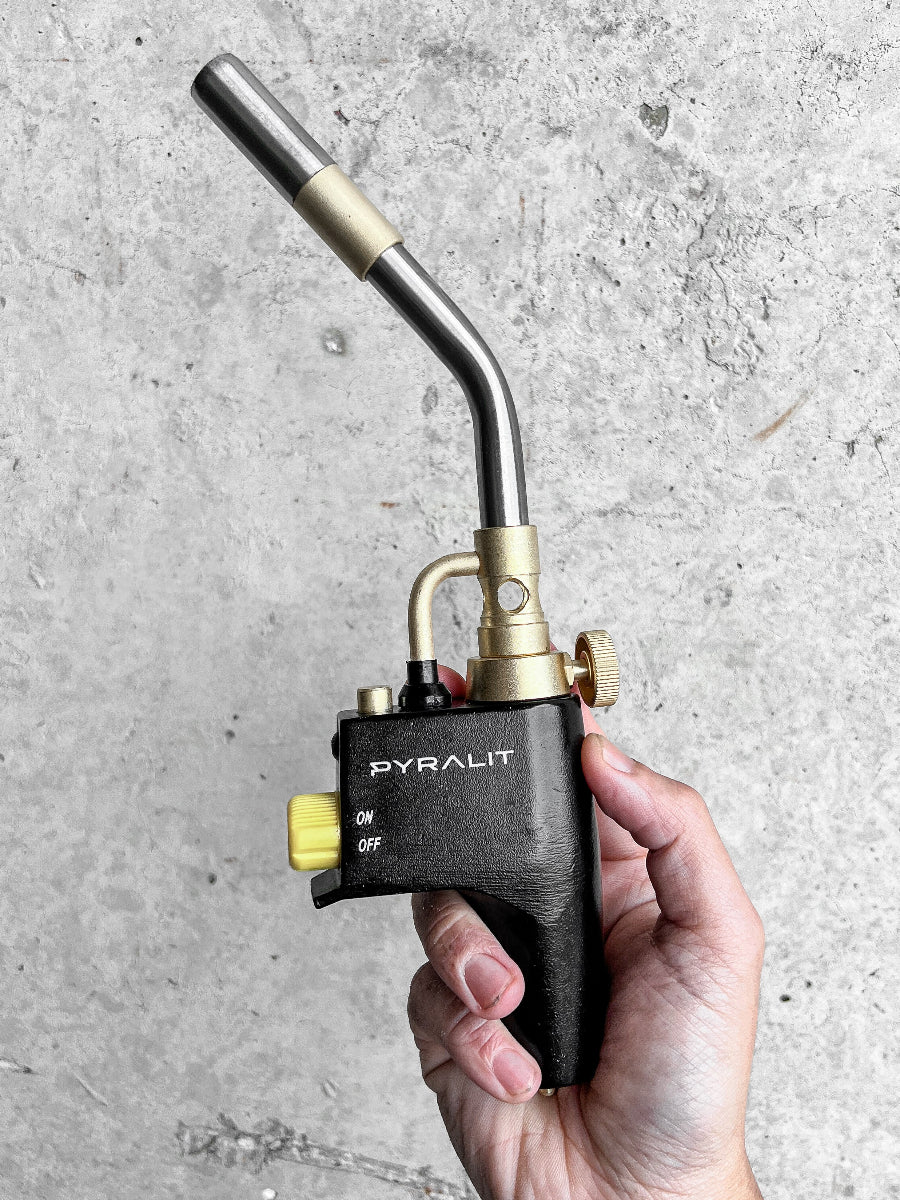 Hand holding a Pyralit torch against a gray concrete background