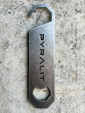 Metal bottle opener with 'PYRALIT' engraving on a concrete surface