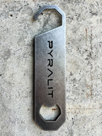 Metal bottle opener with 'PYRALIT' engraving on a concrete surface