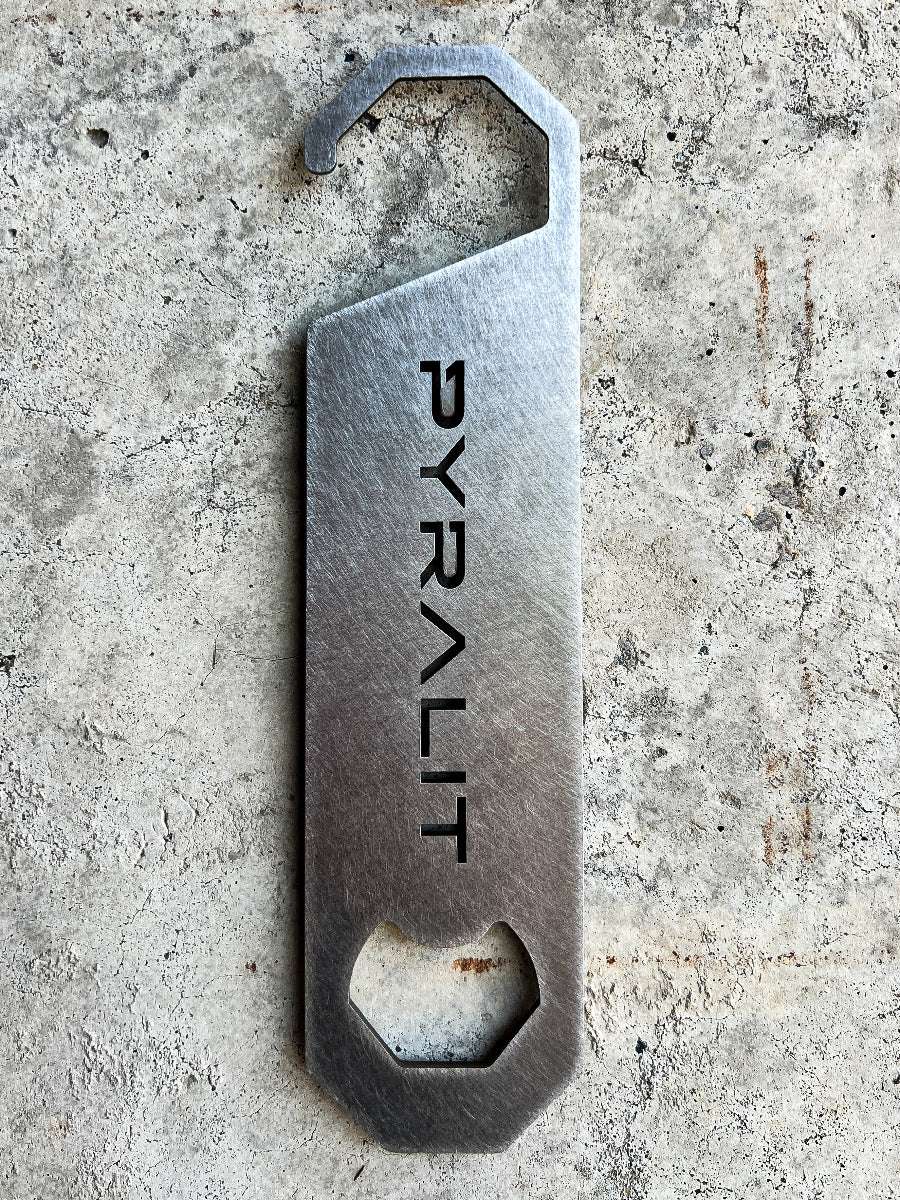 Metal bottle opener with 'PYRALIT' engraving on a concrete surface