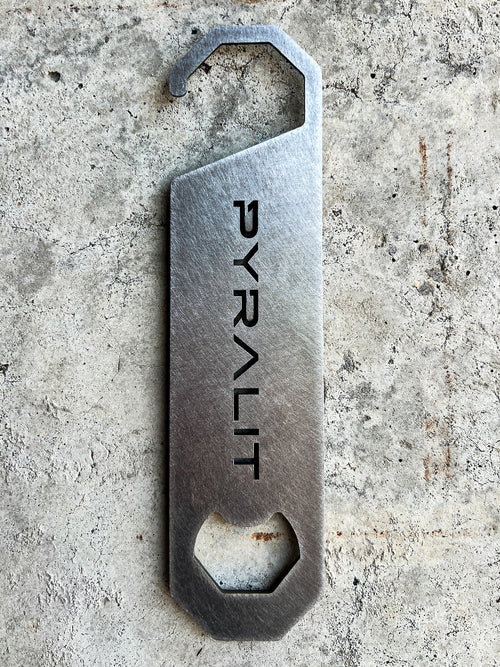 Metal bottle opener with 'PYRALIT' engraving on a concrete surface