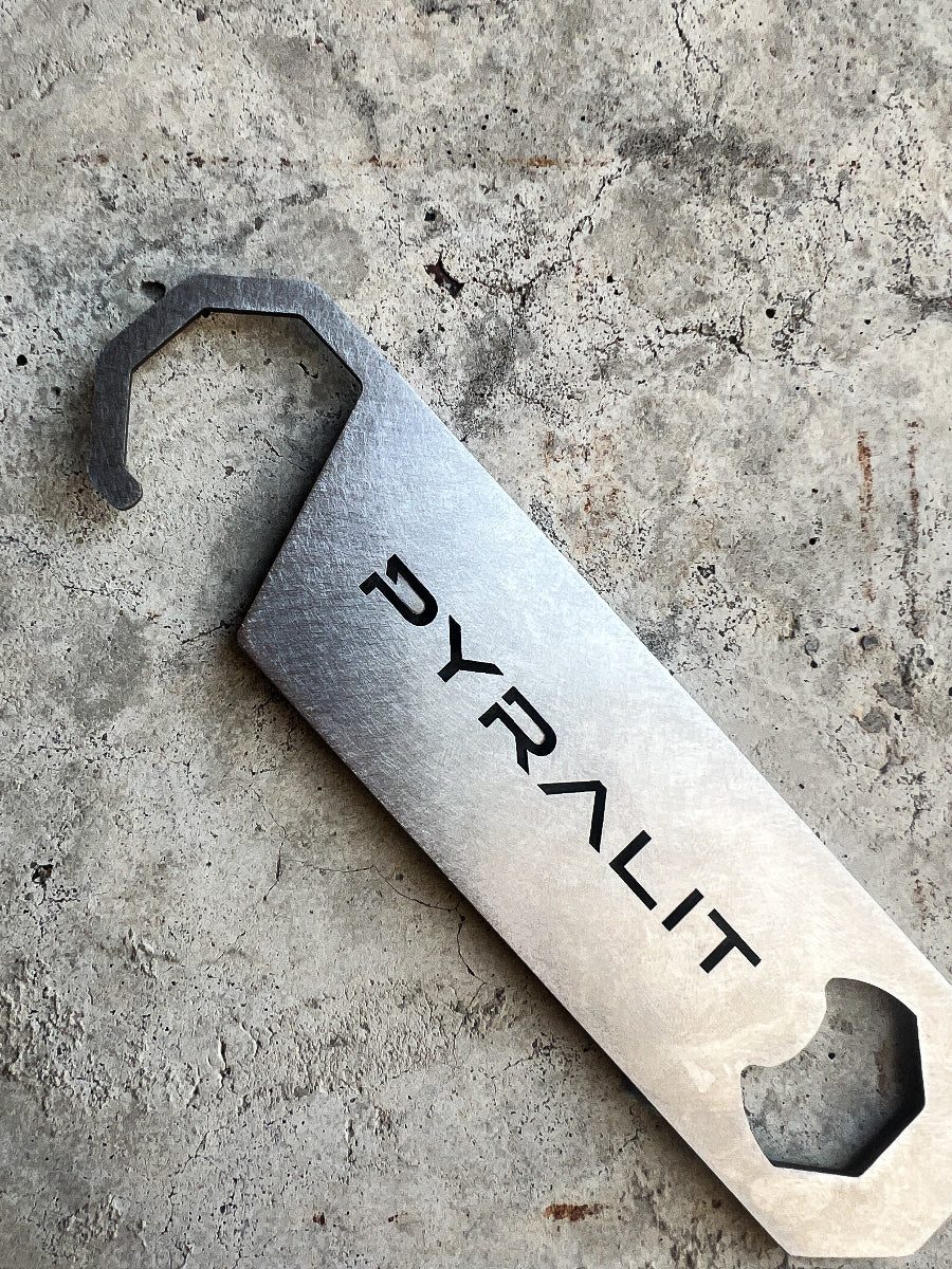 Metal bottle opener with 'PYRALIT' branding on a concrete surface