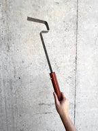 Hand holding a metal tool with wooden handle against a concrete wall
