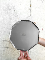 Person holding a metallic octagonal object with a brand logo on a concrete surface